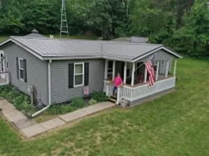 Single-story gray vinyl-sided home with dark gray standing-seam metal roof and white-railed front porch