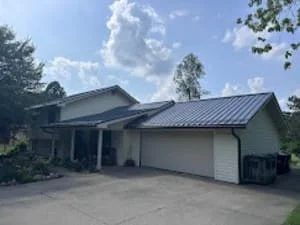 Two-story home with dark gray standing seam metal roof, light siding, and attached white garage door