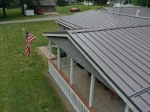 Gray standing seam metal roof over a home with covered front porch and white railings